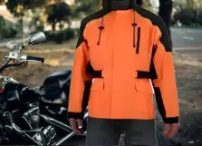 Person wearing an orange and black jacket standing next to a motorcycle.