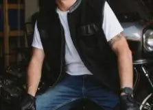 Person wearing a black vest and gloves sitting on a motorcycle.