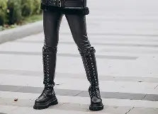 Person wearing black knee-high boots with decorative elements on a city street.
