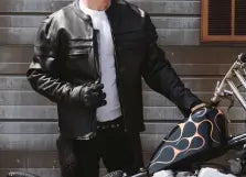 Person wearing a leather jacket standing next to a motorcycle indoors.